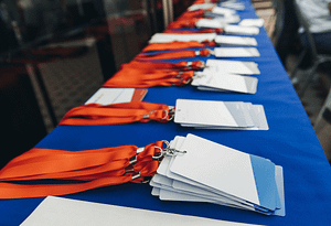 Cordões de crachá com cartões de identificação organizados sobre uma mesa azul, alinhados para evento corporativo.