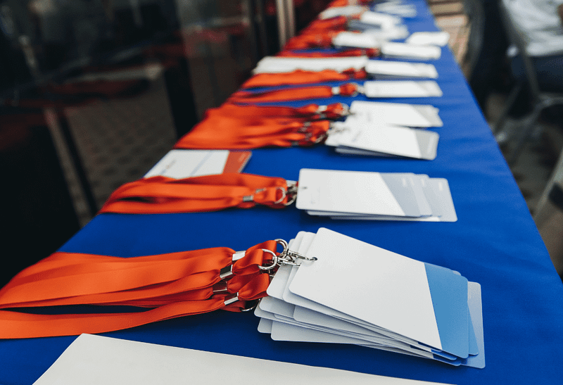 Cordões de crachá com cartões de identificação organizados sobre uma mesa azul, alinhados para evento corporativo.