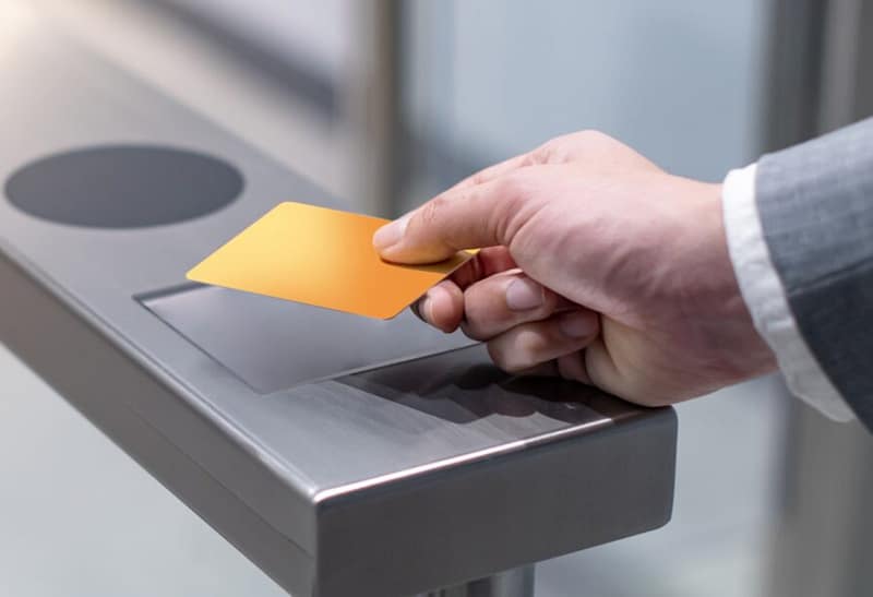 Mão aproximando cartão de acesso de um leitor eletrônico em catraca moderna